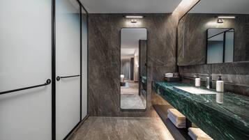 Un baño moderno con un espejo grande, baldosas de mármol oscuro y un tocador elegante.