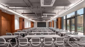Uma sala de conferências com mesas e cadeiras, grandes janelas e vista para edifícios.