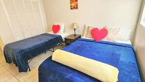 Two beds with blue bedding, a white closet, a nightstand with a lamp, and a heart-shaped pillow.