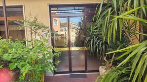 Een gebouwde ingang met een glazen deur, een metalen hek en omliggend groen.