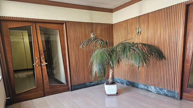 Een hotelkamer met een houten deur, een potpalm en een marmeren vloer.