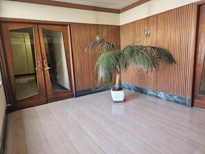 Hotellihuone, jossa on puinen ovi, ruukussa oleva palmu ja marmorilattia.