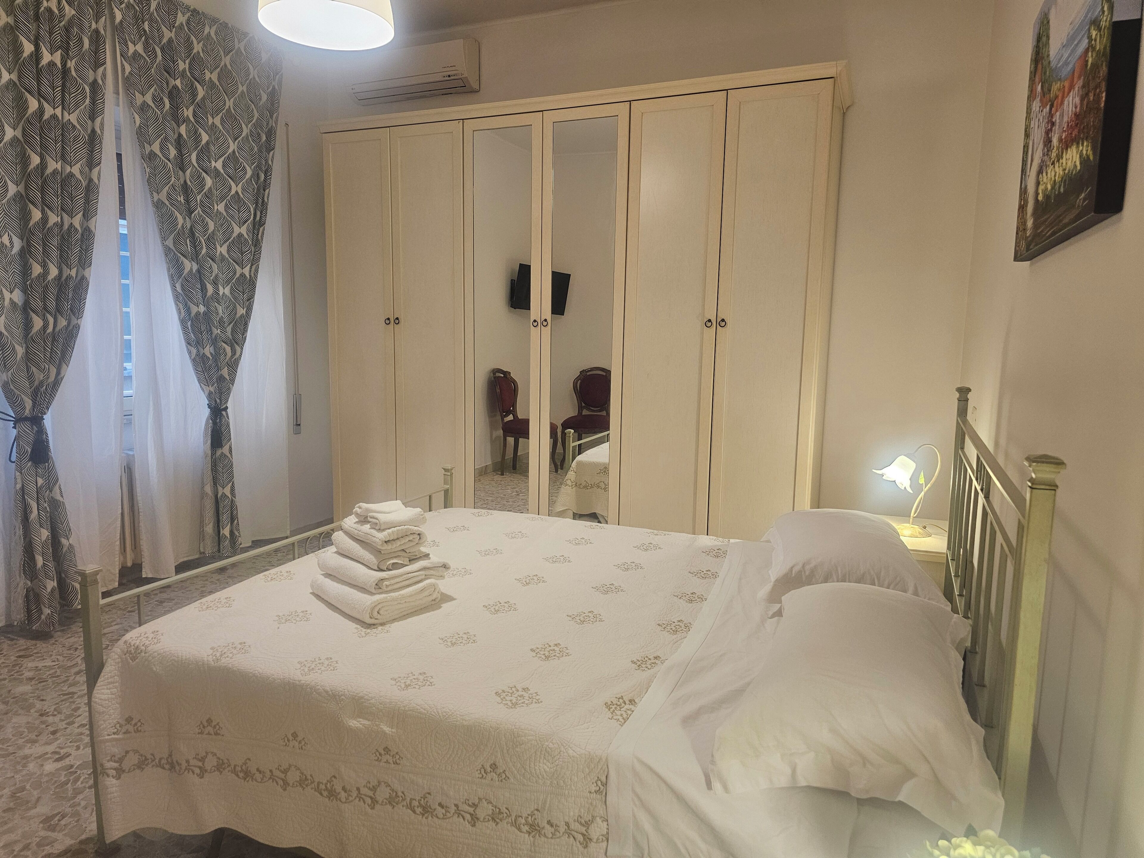 Ein Schlafzimmer mit Bett, Kleiderschrank, Spiegel und Nachttisch mit Lampe.