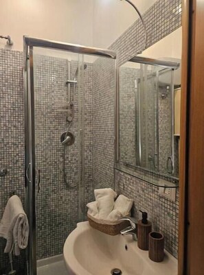 Eine gläserne Dusche mit gefliesten Wänden, ein Waschbecken mit Spiegel und ein Handtuchhalter.