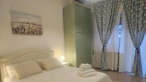 Een net opgemaakt bed met kussens, een groene garderobe en een schilderij aan de muur.