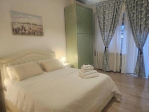 Ein ordentlich bezogenes Bett mit Kissen, ein grüner Kleiderschrank und ein Gemälde an der Wand.