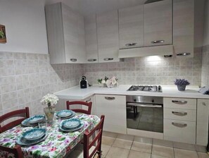 Eine Küche mit weißen Schränken, einem Esstisch mit Blumenmuster-Tischdecke und einem Gasherd.