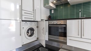 Een compacte keuken met een ingebouwde wasmachine, oven en een groene betegelde achterwand.