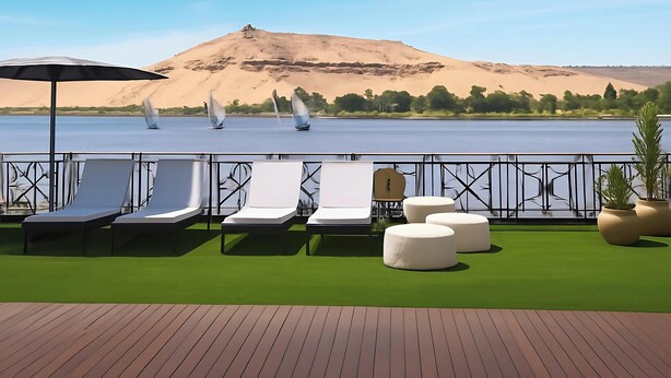 A deck with lounge chairs and ottomans, a water view, and a sandy hill in the background.