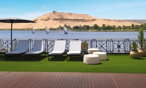 A deck with lounge chairs and ottomans, a water view, and a sandy hill in the background. - 4 nights Aurora Nile Cruise full board (Luxor)