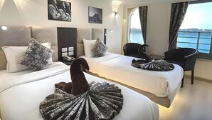 A hotel room with two beds, a desk, a chair, and a view of the water.