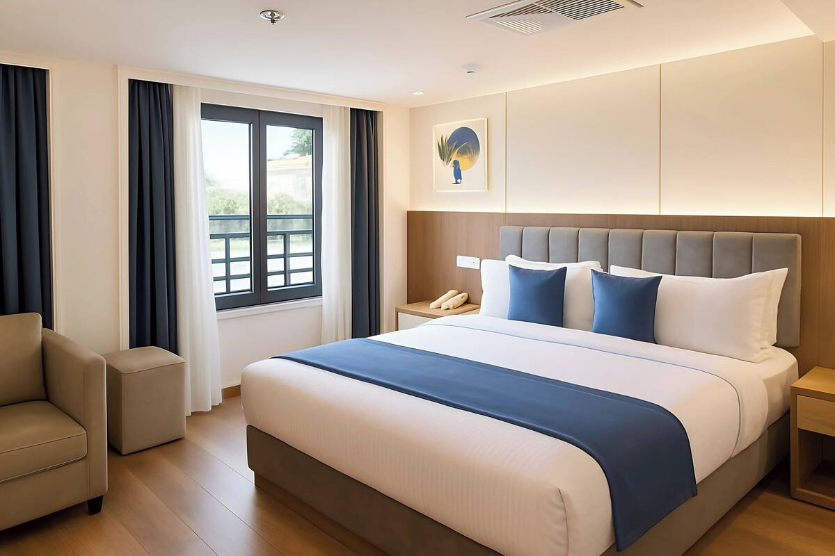 Habitación de hotel moderna con una cama grande, una mesita de noche con teléfono, una silla y una ventana con cortinas.