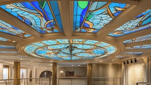 A multi-level hotel interior with a central atrium, a glass staircase, and a chandelier.