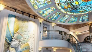 A hotel lobby with a mural, a staircase, and a chandelier.