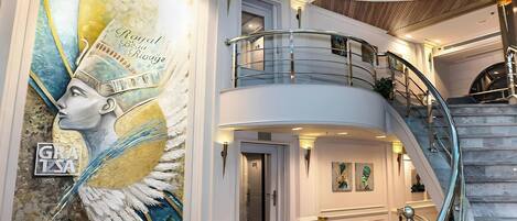A grand interior with a staircase, a mural, and a stained glass ceiling.