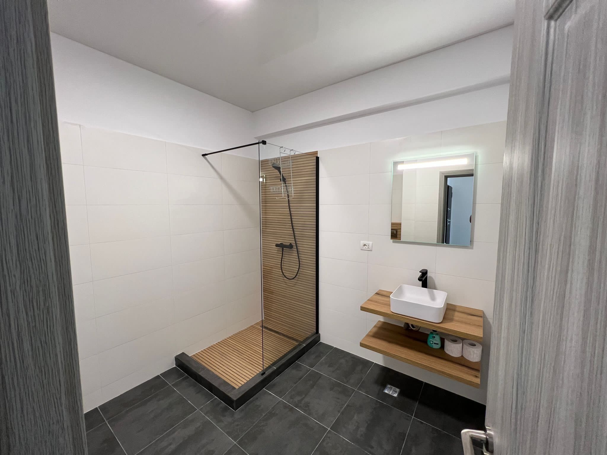 Une salle de bain moderne avec une douche à parois de verre, un meuble-lavabo en bois et un miroir.