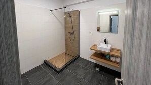 Un bany modern amb plat de dutxa de vidre, un tocador de fusta i un mirall.