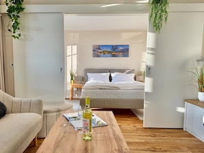 Ein modernes Schlafzimmer mit Bett, Nachttischen, einem Holztisch mit Flasche und Gläsern sowie einem Bild an der Wand.