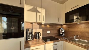 Een moderne keuken met een inbouwoven, een koffiezetapparaat, een waterkoker en een spoelbak.