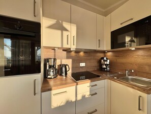 A modern kitchen with a built-in oven, a coffee maker, a kettle, and a sink. - Komfortable Ferienwohnung in Sellin mit Balkon (Sellin)