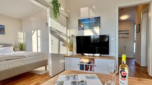 Een moderne hotelkamer met een bed, televisie, boekenplank en een fles wijn op een houten tafel.
