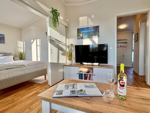A modern hotel room with a bed, TV, bookshelf, and a wine bottle on a wooden table. - Komfortable Ferienwohnung in Sellin mit Balkon (Sellin)