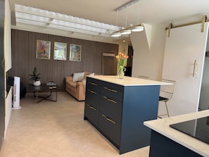 A modern kitchen with a central island, a dining area with a sofa, and a wall with vertical blinds.