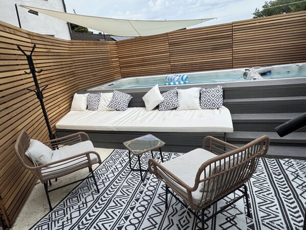 A rooftop patio with a hot tub, cushioned seating, and wicker furniture.