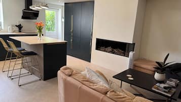 A modern kitchen with a central island, a dining area with chairs, a sofa, and a fireplace.