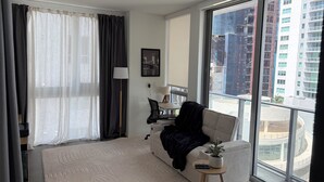 Ein modernes Hotelzimmer mit großem Fenster, einer Couch, einem kleinen Tisch mit Pflanze und einem Schreibtisch mit Lampe.