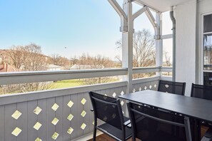 Eine überdachte Terrasse im Freien mit Tisch und Stühlen, Blick auf die Umgebung und einem Geländer mit rautenförmigen Aussparungen.