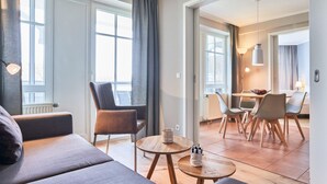 Ett modernt vardagsrum med en soffa, fåtöljer, ett matbord och en köksdel med utsikt över omgivningen.
