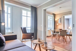 Ein modernes Wohnzimmer mit Sofa, Stühlen, einem Esstisch und einer Küchenzeile mit Blick ins Freie.