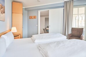 Ein Hotelzimmer mit Bett, Stuhl, Lampe, Kleiderschrank und Blick ins Freie.