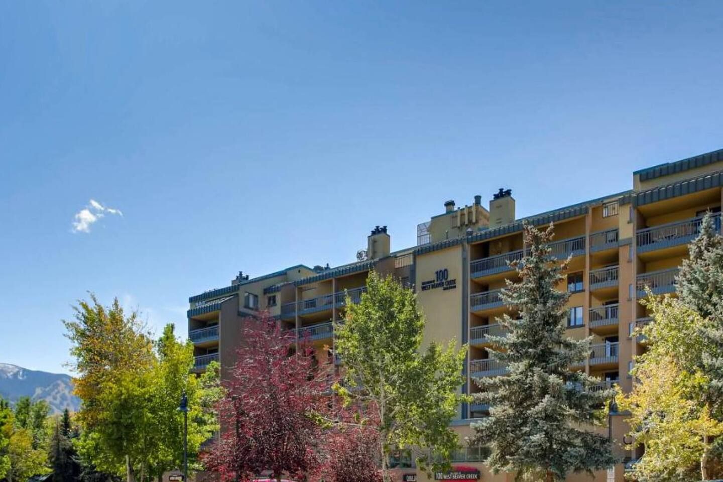 Un hôtel à plusieurs étages, doté de balcons, entouré d’arbres et offrant une vue sur un ciel dégagé.
