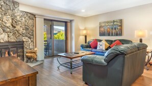A living room with a stone wall, a fireplace, a sofa with cushions, a coffee table, and a painting on the wall. - Ski Beaver Creek | Walk to Gondola (Avon)