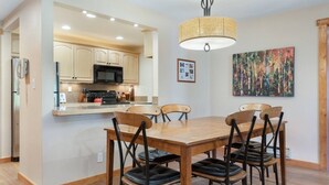 A dining area with a wooden table and chairs, a kitchen with light-colored cabinets, and a hanging light fixture. - Ski Beaver Creek | Walk to Gondola (Avon)