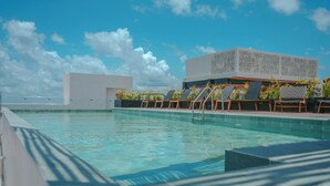 Ein Pool auf dem Dach mit Liegestühlen und einem modernen Gebäude im Hintergrund.