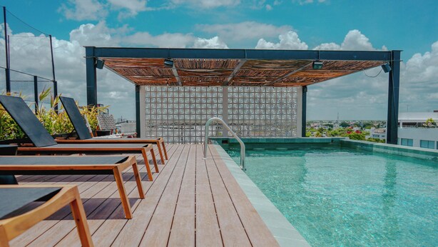 Ein Pool auf dem Dach mit Holzterrasse, Liegestühlen und einer Wand mit Muster im Hintergrund.