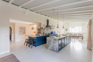 A modern kitchen with a marble island, pendant lights, and a view into the dining area.