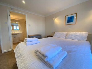 Een slaapkamer met een bed, nachtkastje, nachttafel, een ingelijste foto aan de muur en een open deur naar een badkamer.