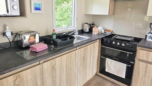 Moderni keittiö, jossa on sisäänrakennettu uuni, liesi, pesuallas ja ikkuna, josta avautuu näkymä vehreään maisemaan.