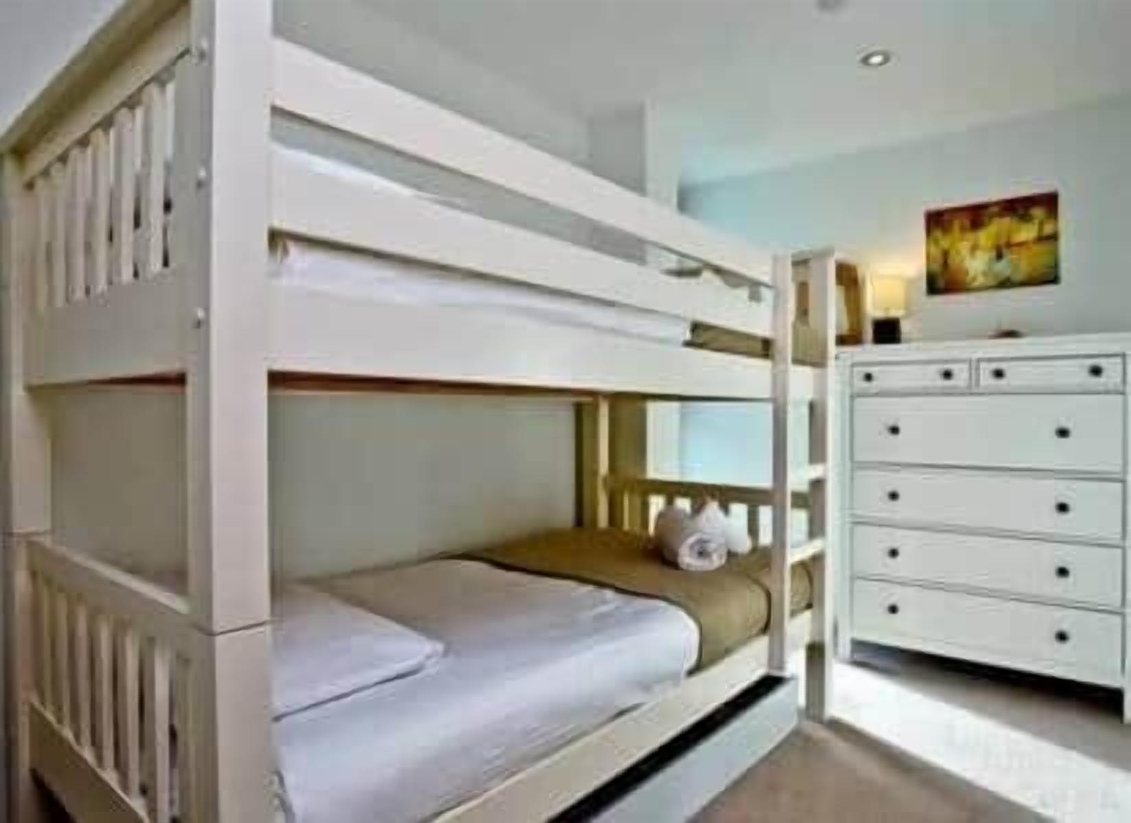 A bunk bed with a white dresser and a painting on the wall.