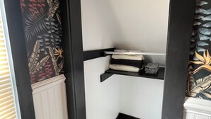 Un petit espace de rangement fermé, avec des étagères noires, un radiateur blanc et un papier peint à motifs.