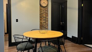 Un coin repas avec une table ronde en bois, des chaises noires, une horloge murale et un luminaire moderne au plafond.