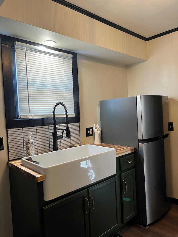 Una cocina con un lavabo blanco, grifo negro y un refrigerador de acero inoxidable.