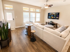 A living room with a sectional sofa, a TV mounted on the wall, a ceiling fan, and a large window with blinds. - Peaceful Escape | Backyard | Community Pool & Park (Midlothian)