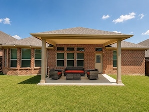 A covered patio area with a sofa and two chairs, a brick building with a pitched roof, and a clear blue sky. - Peaceful Escape | Backyard | Community Pool & Park (Midlothian)