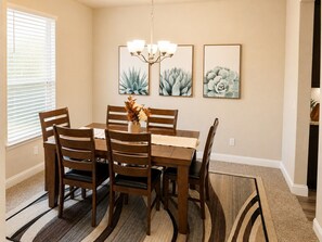 A dining area with a wooden table and chairs, a chandelier, and three framed botanical prints on the wall.