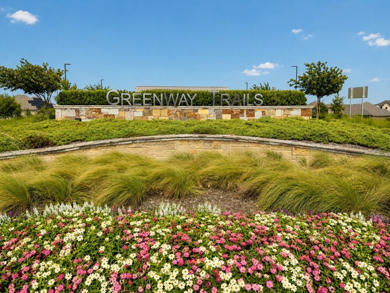 Zona ajardinada con un letrero que dice 'GREENWAY TRAILS' y una variedad de flores.